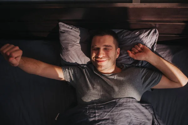 Un hombre en su cama por la mañana. Se está estirando. Gran comienzo del día Fotos De Stock