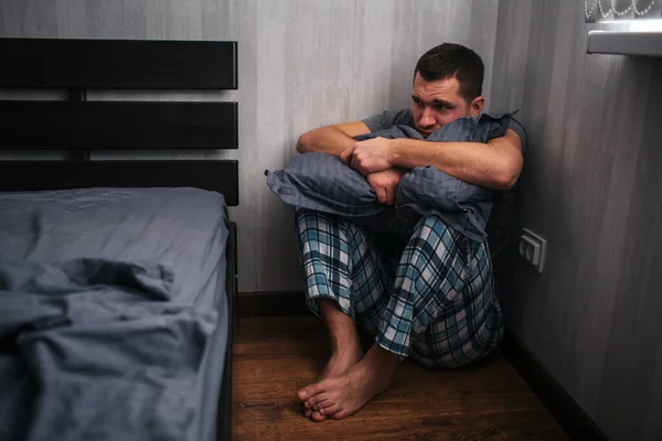 Depresszió, pánikroham. Egy férfi ül egy sarokban az ágy mellett. Rosszul érzi magát. Stock Fotó