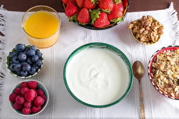 Breakfast table with natural yogurt, berries, marmalade, orange juice and nuts over a white nap