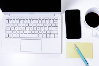 Laptop, akıllı telefon kalemi ve kahve fincanı beyaz bir masanın üstünde.