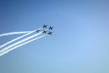 Mavi gökyüzüne doğru uçan beş uçak. Bir uçak diğerlerinin etrafında bir fıçı akrobatik figür oluşturuyor. Moldova 'daki Chisinau Havaalanı' nda hava gösterisi. Arkada yoğun dumanlı uçaklar var..