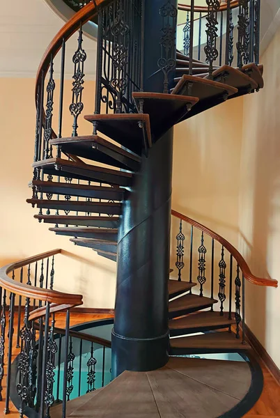 stock image Beautiful vintage spiral staircase in brown wood with ornate black metal columns. Vertical view. White-cream wall.