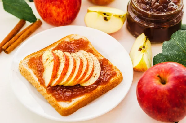 Roti panggang dengan selai apel hancur, irisan apel segar, kayu manis di atas piring di atas meja putih. Apel dan selai apel dalam toples. Konsep ini . — Stok Foto