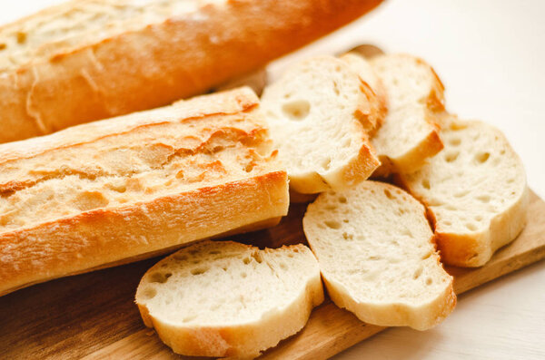 Fresh baguettes with crispy crust chopped on a cutting board on a white table. Tasty breakfast.