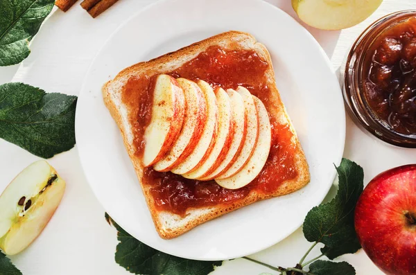 Roti panggang dengan selai apel hancur, irisan apel segar, kayu manis di atas piring di atas meja putih. Apel dan selai apel dalam toples. Konsep. Sarapan manis yang lezat. Tampilan atas . — Stok Foto