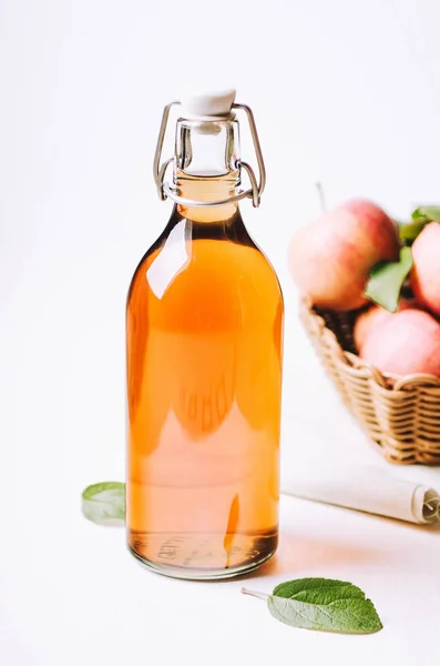 Cuka apel dalam botol di atas meja kayu putih dengan apel dalam keranjang . — Stok Foto