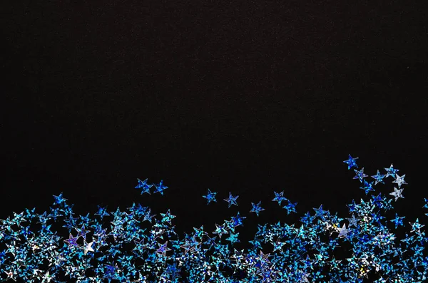 Shiny blue stars of foil on black background. Festive confetti.