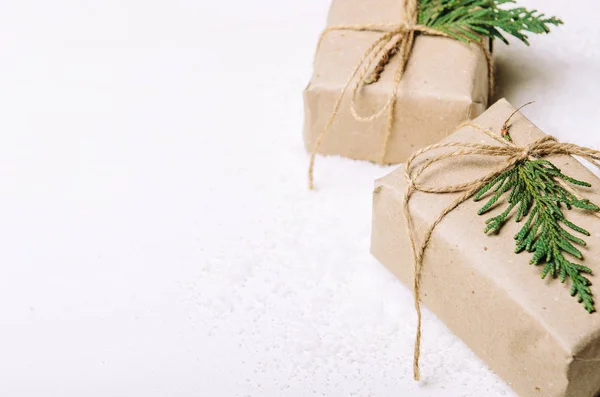 Cajas de regalo en papel kraft y ramas de abeto sobre fondo blanco y nieve artística. Estilo rústico. Copiar espacio — Foto de Stock