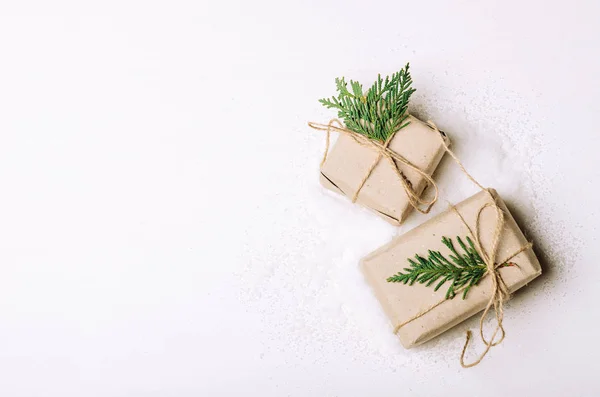 Scatole regalo in carta kraft e rami di abete su sfondo bianco e neve abile. Stile rustico. Copia spazio, disposizione piatta . — Foto Stock