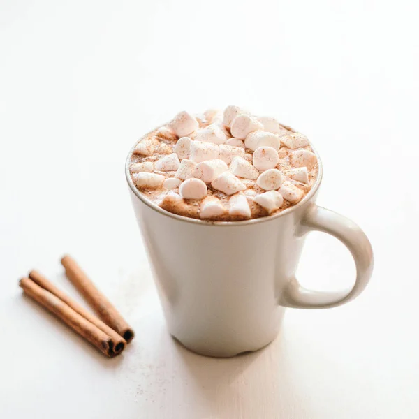 Ζεστό κακάο με γλυκό marshmallow και κανέλα στο λευκό τραπέζι. Ένα γλυκό ποτό. — Φωτογραφία Αρχείου