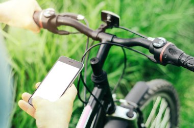 Orman yolunda dağ bisikleti üzerinde oturan erkek eller akıllı telefon tutuyor. Konsept navigasyon, yaz aktif spor, teknoloji