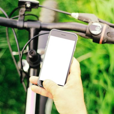 Orman yolunda dağ bisikleti üzerinde oturan erkek eller akıllı telefon tutuyor. Konsept navigasyon, yaz aktif spor, teknoloji