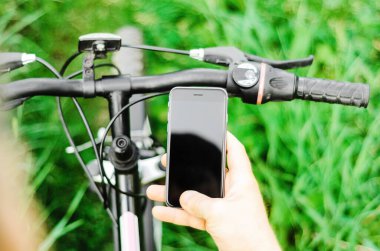 Orman yolunda dağ bisikleti üzerinde oturan erkek eller akıllı telefon tutuyor. Konsept navigasyon, yaz aktif spor, teknoloji
