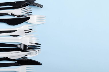Mavi arka planda plastik beyaz ve siyah tek kullanımlık çatal ve bıçaklar. Plastik tabaklar. Boşluğu kopyala, üst görünüm, düz uzanma