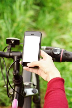 Orman yolunda bir dağ bisikletinin üzerinde otururken akıllı telefon tutan kadın eller. Konsept navigasyon, yaz aktif spor, teknoloji