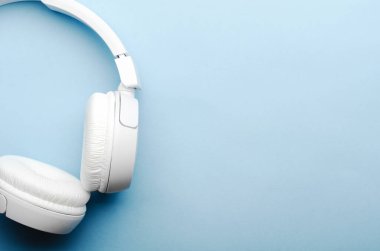 Mavi arka planda beyaz kablosuz bluetooth kulaklıklar. Yakın plan, kopyalama alanı, üst görünüm, düz çizgi