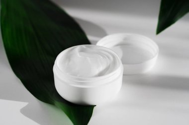 Kapalı krema kavanozu açılır ve yapraklar yan görünür. Organik kozmetik, doğal kozmetik botanik konsepti. Kadın cilt bakım ürünü. Yüz bakımı, vücut kremi plastik kap ve yaprak bileşimi..