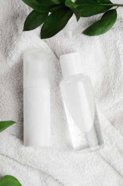 Micellar su ve losyon üst görünüm. Yeşil yapraklı beyaz havluyla kozmetik ürünleri. Plastik kapta sıvı makyaj çıkarıcı. Doğal malzemeli sıvı temizlik losyonu..