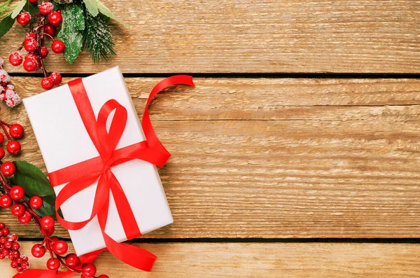 Hediye kutusu ve Holly Ilex 'in böğürtlenleri. Yeni yıl, Noel hediyesi. Telif alanı olan şenlikli ahşap zemin. Dekoratif unsurlu Noel kompozisyonu. Kış tatili kavramı.