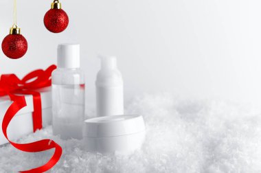 Cilt kozmetik şişeleri stilize kar kaplı yüzeyde. Kırmızı kurdeleli beyaz hediye kutusu ve gösterişli dekoratif arka plan. Yeni yıl ve Noel zamanı kadın fikri sunar.