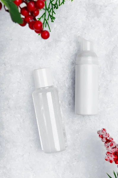 スキンケア製品のフラット雪の背景に横たわっていた 装飾的な赤い果実を背景にした顔のクレンザーとミセルウォーターボトルのモックアップ テキストスペース付き冬の化粧品広告 — ストック写真