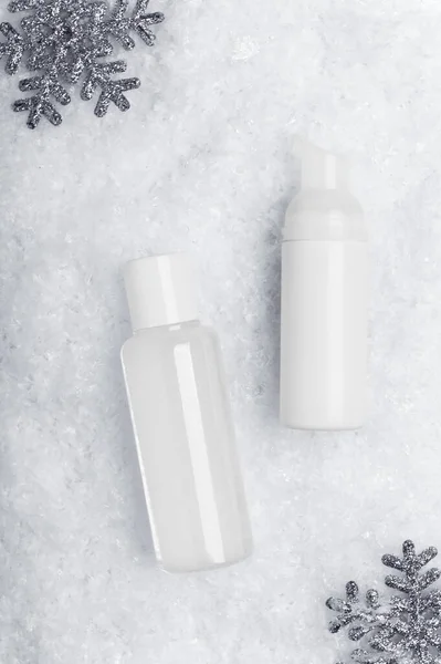 スキンケア製品のフラット雪の背景に横たわっていた 装飾的な銀の雪片の背景と顔のクレンザーとミセルウォーターボトルのモックアップ テキストスペース付き冬の化粧品広告 — ストック写真