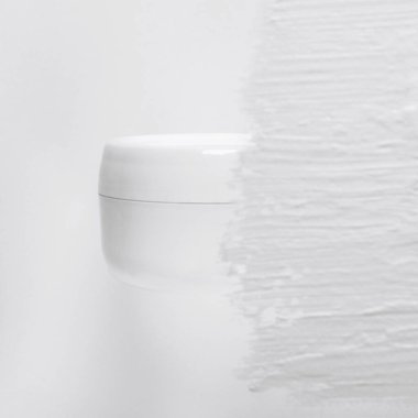 Bulanık doku arka planında kozmetik krem kavanozu modeli. Süslü makyaj ürünleri konteynırı kremalı arkaplanda izole edilmiş. Odaklanmamış beyaz boya fırçası darbeleri. Yüz derisi, maske yakın plan..