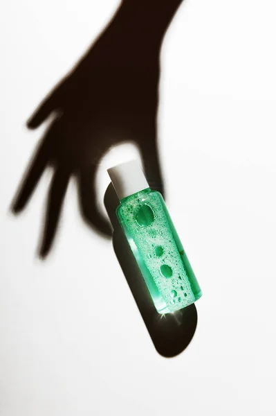 El gölgesi kozmetik sıvı şişe bileşimi tutuyor. Makyaj temizleme ürünü paketi, oje yeşili temizleme modeli. Cilt bakımı losyonu. İşaretlenmemiş şişe ile arka plan.