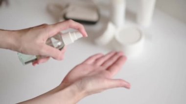 Masada elinde kozmetik ürünleri olan bir kadın ellerine antiseptik losyon sürüyor. Evde bakterilere karşı korunmak için şeffaf bir doz şişesinde alkol çözeltisi. Kozmetik güzellik ürünleri temizleniyor