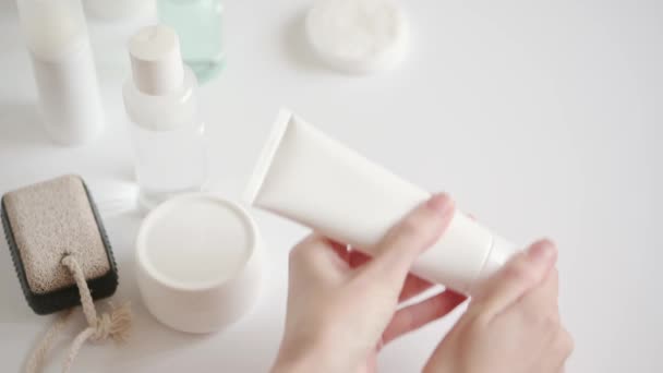 Het meisje neemt een plastic pakket met room en knijpt het cosmetische product op haar handen. Wrijven moisturizer om de huid te hydrateren. Home huidverzorging in quarantaine, isolatie — Stockvideo