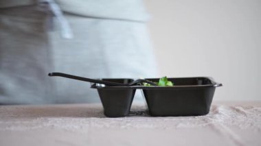 Bir kadın masaya bir teslimat servisinden taze salata ile plastik bir kap koyar. Evde diyet yemek yemek. Mutfakta beslenme çantasından alınmış sebzeli sağlıklı bir atıştırma..