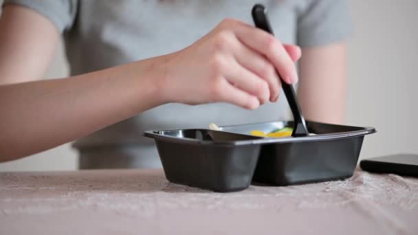 Seorang wanita menaruh wadah plastik dengan salad sehat di atas meja dan makan. Tangan wanita dengan garpu close-up. Makanan siap saji buatan sendiri dikirim dari restoran, dipesan melalui telepon. Makanan ringan sehat, diet.. — Stok Video