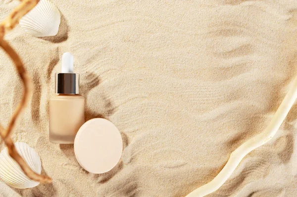 Facial foundation glass bottle cream. Closed container of liquid tone. Unbranded flacon of correction cosmetic product with cotton sponge on seashore backdrop. Beauty and cosmetology branding concept.