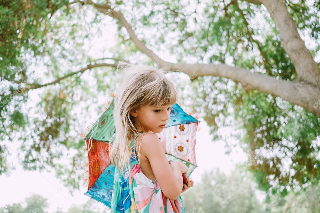 Little girl holding a colorful sun umbrella in the summer in the park