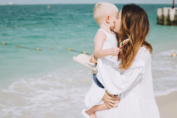 Young mother carring her little son at sandy beach in Dubai, UAE