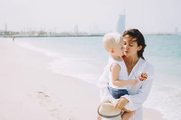 Young mother carring her little son at sandy beach in Dubai, UAE