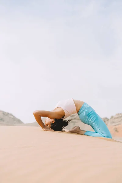 Young woman doing yoga in desert with mountains at sunrise