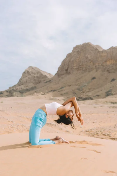 Young woman doing yoga in desert with mountains at sunrise