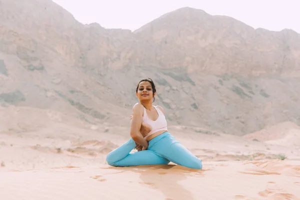 Young woman doing yoga in desert with mountains at sunrise