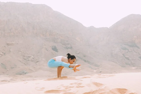 Young woman doing yoga in desert with mountains at sunrise