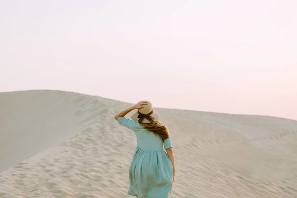 Young woman walking on the sand dunes in the desert during the sunset