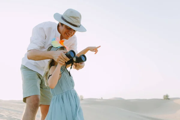 Daddy and daughter standing in the desert and looking though the binoculars