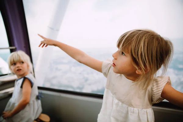Little girl pointing her finger and showing something in a ferris wheel cabin