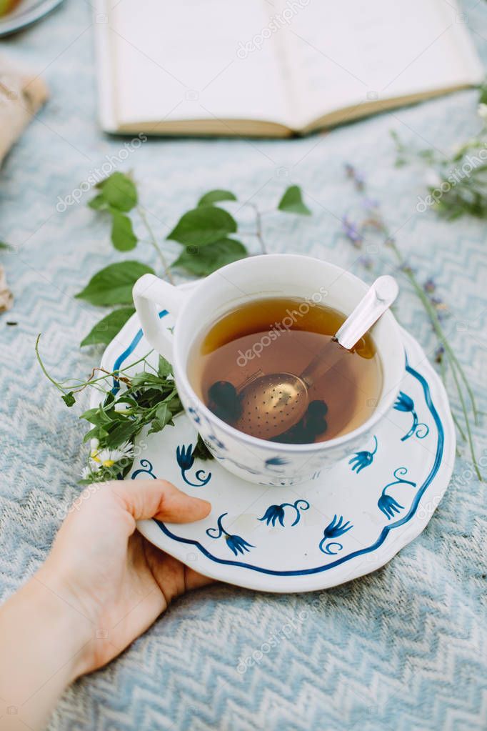 Hand golding a cup of tea outdoor with a picnic on the background