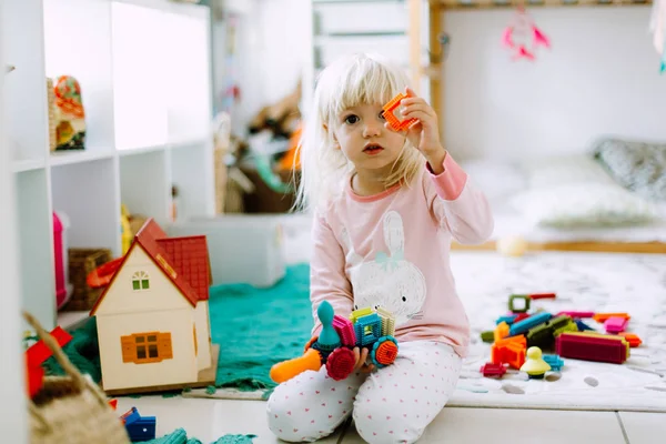 Маленькая девочка играет с цветными строительными деталями на полу дома — стоковое фото