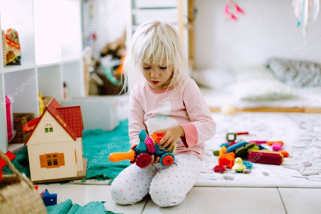 Little girl playing with colored construction details on the floor at home