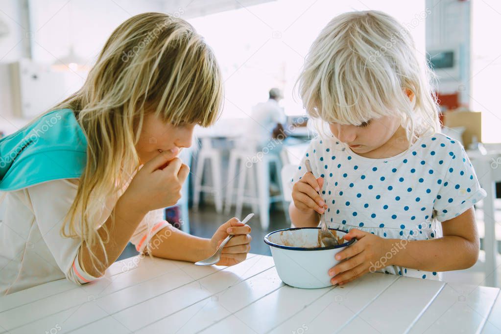 Two girls sisters eating ice cream from one bowl in a cafe indoors