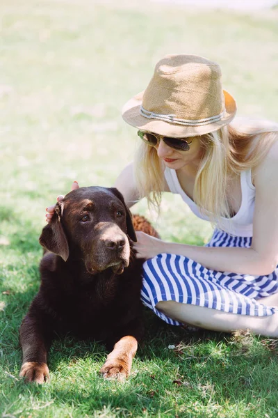 Mujer joven sentada junto a un perro grande y lo acaricia —  Fotos de Stock