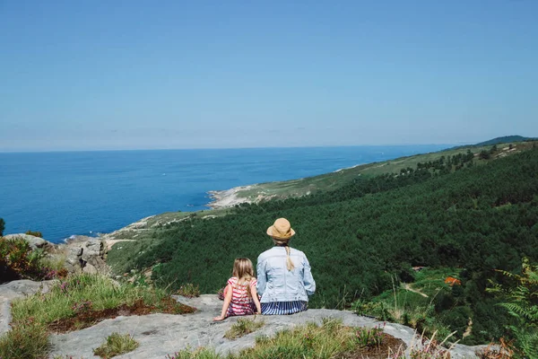 Mother and daughter sitting on the cliff admiring the ocean in Spain — Stock Photo, Image