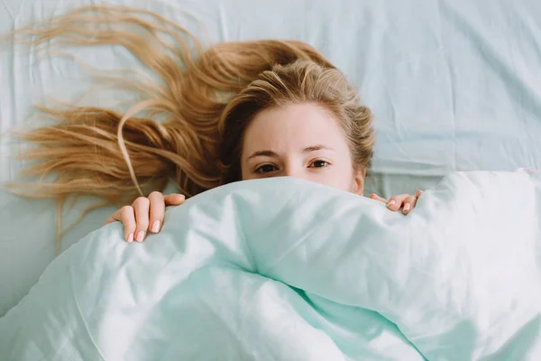 Mulher na cama e meia cara escondida sob uma roupa de cama — Fotografia de Stock